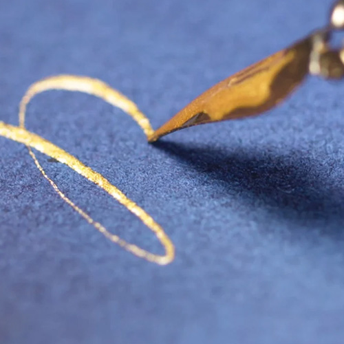 an artist creating calligraphy, with gold ink on r